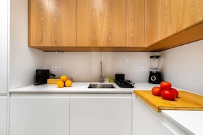 A kitchen with white cabinets, a wooden countertop, a sink, a Bosch blender, and a cutting board with tomatoes and oranges. - Cozy Retreat Near Picturesque Rua Verde (Lisboa)