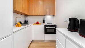 A modern kitchen with white cabinets, a black oven, a coffee maker, and a blender on the counter. - Cozy Retreat Near Picturesque Rua Verde (Lisboa)