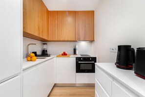 A modern kitchen with white cabinets, a black oven, a coffee maker, and a blender on the counter. - Cozy Retreat Near Picturesque Rua Verde (Lisboa)