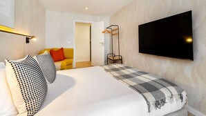 A modern hotel room with a large bed, a flat-screen TV mounted on the wall, a bedside table, and a floor lamp. - Cozy Retreat Near Picturesque Rua Verde (Lisboa)