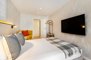 A modern hotel room with a large bed, a flat-screen TV mounted on the wall, a bedside table, and a floor lamp. - Cozy Retreat Near Picturesque Rua Verde (Lisboa)