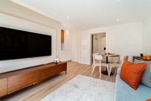 A modern living room with a flat-screen TV, a wooden console, a dining area with a table and chairs, and a sofa with an orange pillow. - Discover Lisbon Steps from Picturesque Rua Verde (Lisboa)