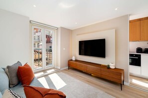 A modern living room with a flat-screen TV, a wooden console table, and a sofa with patterned cushions. - Discover Lisbon Steps from Picturesque Rua Verde (Lisboa)