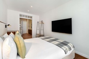 Ein Hotelzimmer mit einem Bett, einem an der Wand befestigten Fernseher, einer Nachttischlampe und einer Tür zu einem Flur.