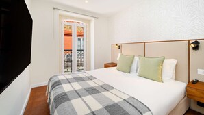 Et hotelværelse med en seng, et natbord, en vægmonteret lampe og en dør, der fører til et udendørs område.