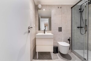 A modern bathroom with a white sink, mirror, and a glass shower enclosure. - Discover Lisbon Steps from Picturesque Rua Verde (Lisboa)