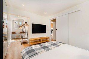 A modern bedroom with a large bed, a flat-screen TV mounted on the wall, a wooden bench, and a clothing rack. - Discover Lisbon Steps from Picturesque Rua Verde (Lisboa)