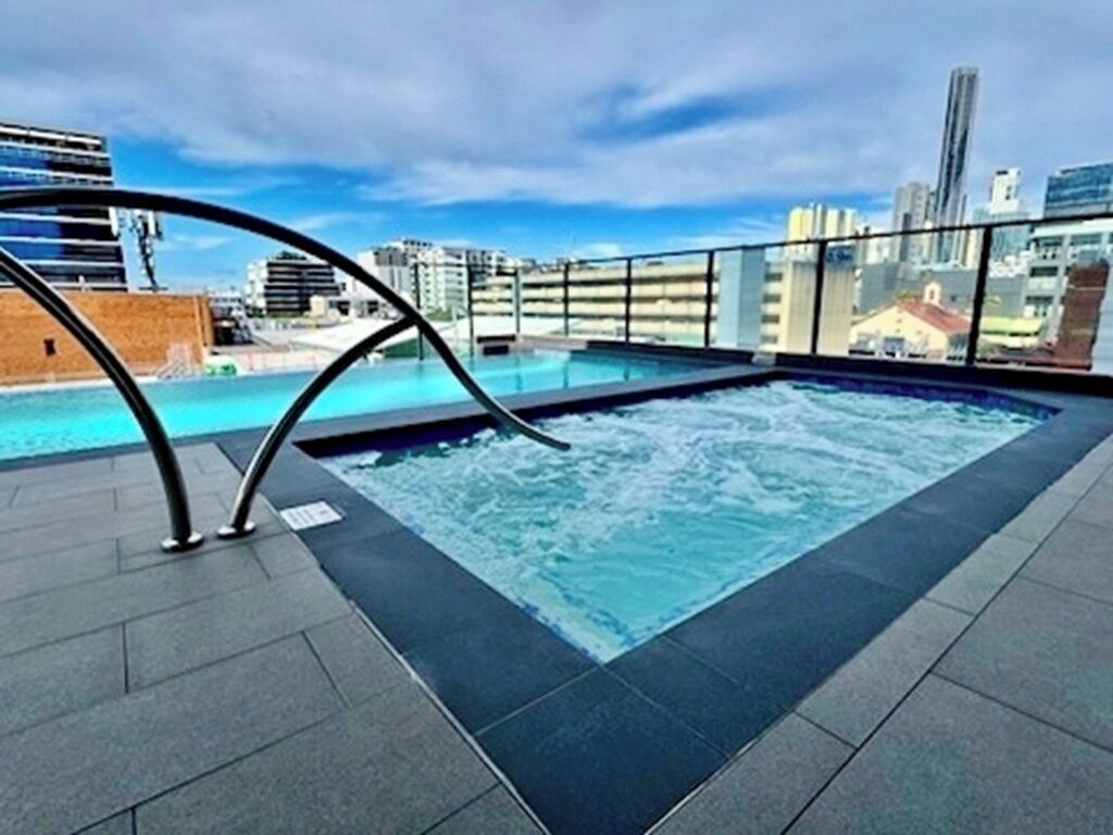 Piscina en la azotea con vista a la ciudad, rodeada por una barandilla de vidrio.
