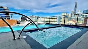 Ein Pool auf dem Dach mit Blick auf die Stadt, umgeben von einem Glasgeländer.