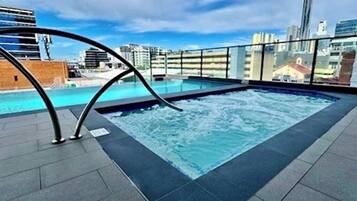 Piscina en la azotea con vista a la ciudad, rodeada por una barandilla de vidrio.