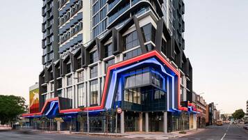A modern building with a curved glass facade, a prominent red and blue entrance, and a large vertical banner on the left side.