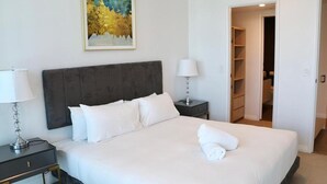 Ein ordentlich bezogenes Bett mit weißen Leinen, ein dunkles Kopfteil, eine Nachttischlampe, ein Nachttisch und ein Bild an der Wand.