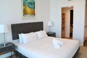 A neatly made bed with white linens, a dark headboard, a bedside lamp, a nightstand, and a painting on the wall. - Fortitude Valley Pool Sauna & Gym (Brisbane)