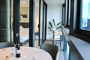 A modern hotel room with a bed, a sitting area with a chair and table, and a balcony with a plant. - Fortitude Valley Pool Sauna & Gym (Brisbane)