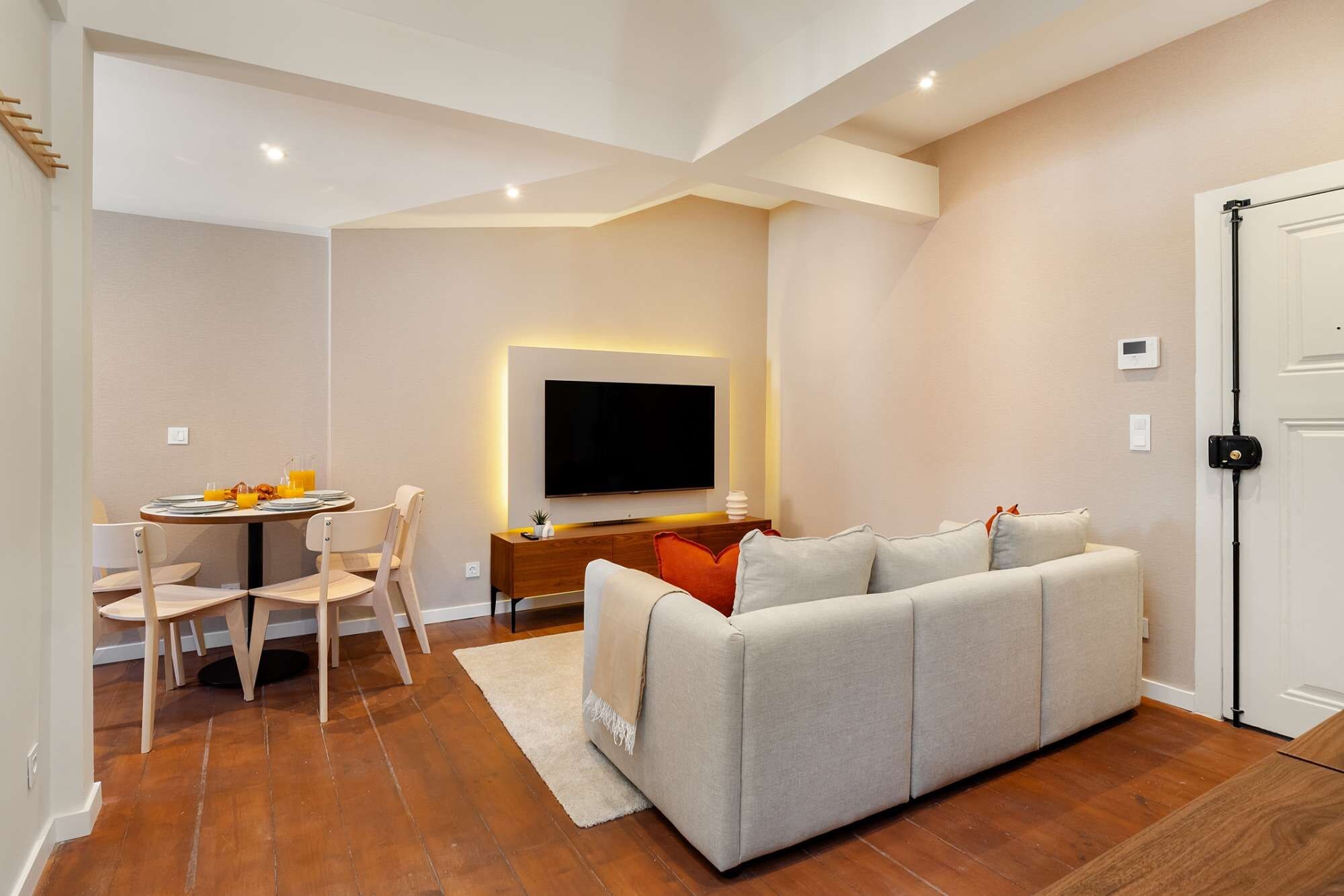A modern living room with a sofa, TV, dining table, and chairs.