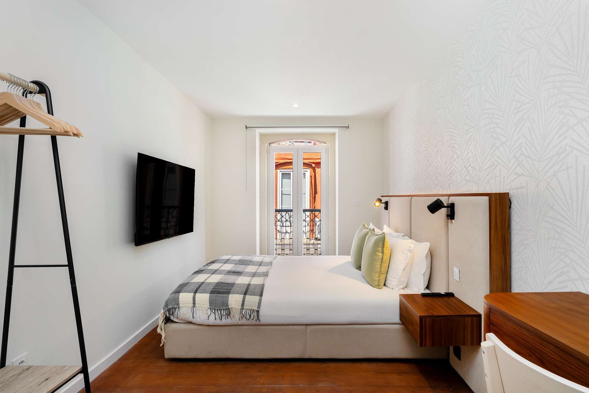 Un dormitorio con una cama, un televisor montado en la pared, una escalera de madera y una mesita de noche de madera.