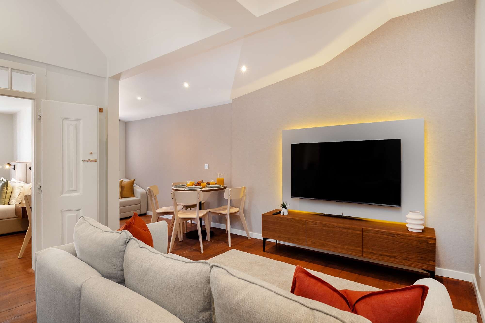 Uma sala de estar moderna com televisão de tela plana na parede, um sofá, uma mesa de jantar com cadeiras e um armário de madeira.