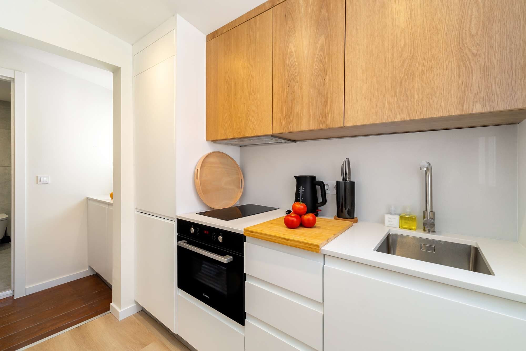 A modern kitchen with white cabinetry, a wooden countertop, a stove, a sink, and a coffee maker.