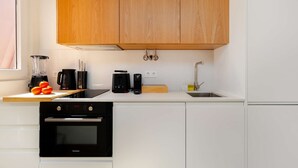 Et moderne køkken med træskabe, indbygget ovn, vask og diverse hårde hvidevarer, herunder en blender og kaffemaskine.