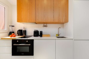 Eine moderne Küche mit Holzschränken, einem Backofen, einer Spüle und verschiedenen Geräten, darunter ein Mixer und eine Kaffeemaschine.