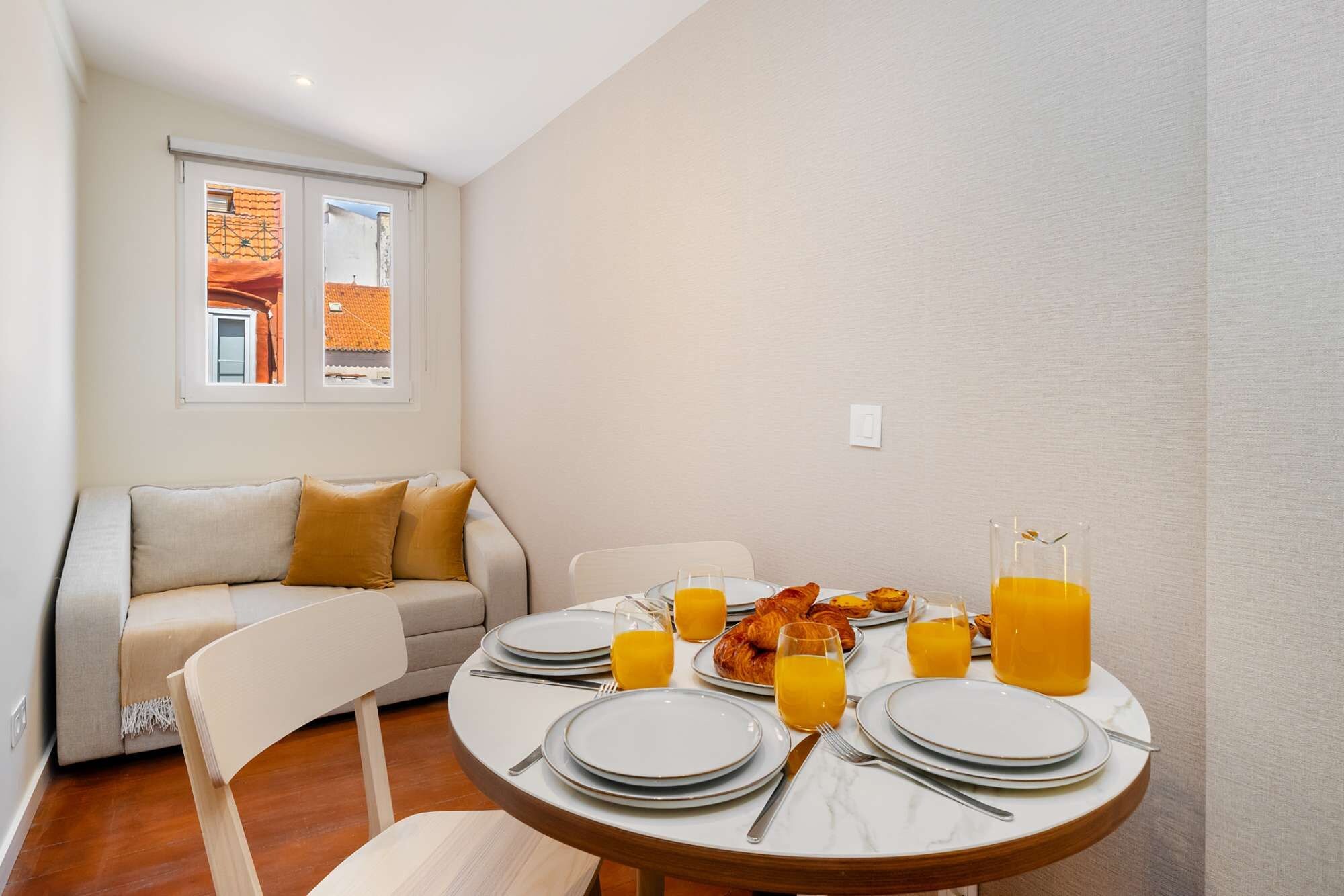 A dining area with a round table set for breakfast, including plates, glasses, and croissants.
