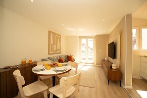 A dining area with a round table, chairs, and a breakfast setup. There is a sofa and a TV mounted on the wall. - Traditional Lisbon Building near Chiado and Santos (Lisbon)