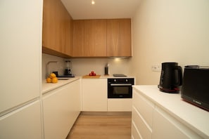 A compact kitchen with wooden cabinets, a built-in oven, a coffee maker, and a cutting board with fruit. - Traditional Lisbon Building near Chiado and Santos (Lisbon)
