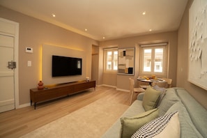 A modern living room with a flat-screen TV, a sofa, a dining area with a table and chairs, and a window with blinds. - Traditional Lisbon Building near Chiado and Santos (Lisbon)