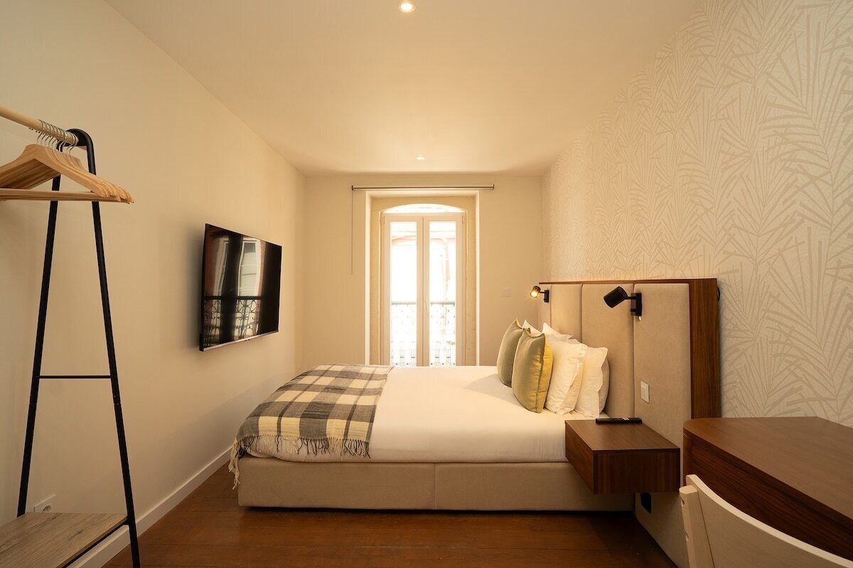 Un dormitorio con cama, mesita de noche, perchero, un cuadro en la pared y una ventana con vistas.