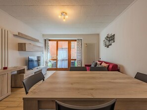 A modern living room with a wooden dining table, a red sofa, and a TV on a wooden stand. - Stefani by Interhome (Lago di Ledro)