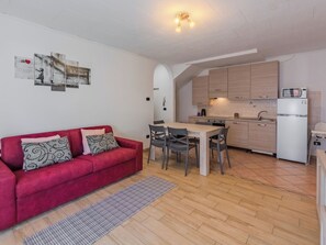 A compact living space with a red sofa, a dining table, and a kitchen area. - Stefani by Interhome (Lago di Ledro)