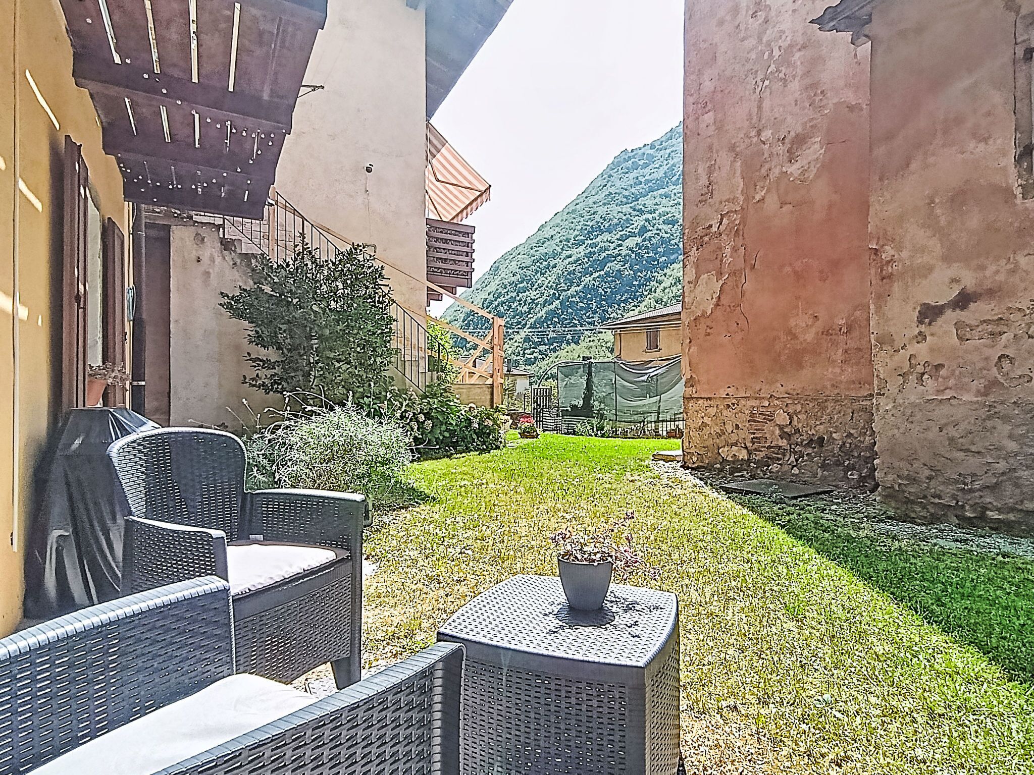 A courtyard with outdoor furniture, a small table with a plant, and a view of a mountain.