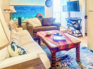 A living room with a sofa, a coffee table, a television, and a dartboard. - Hale Akala - Shared Home & Suite (Kailua-Kona)