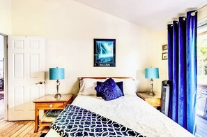 A bedroom with a bed, two bedside tables, a nightstand, a poster on the wall, and a window with curtains.
