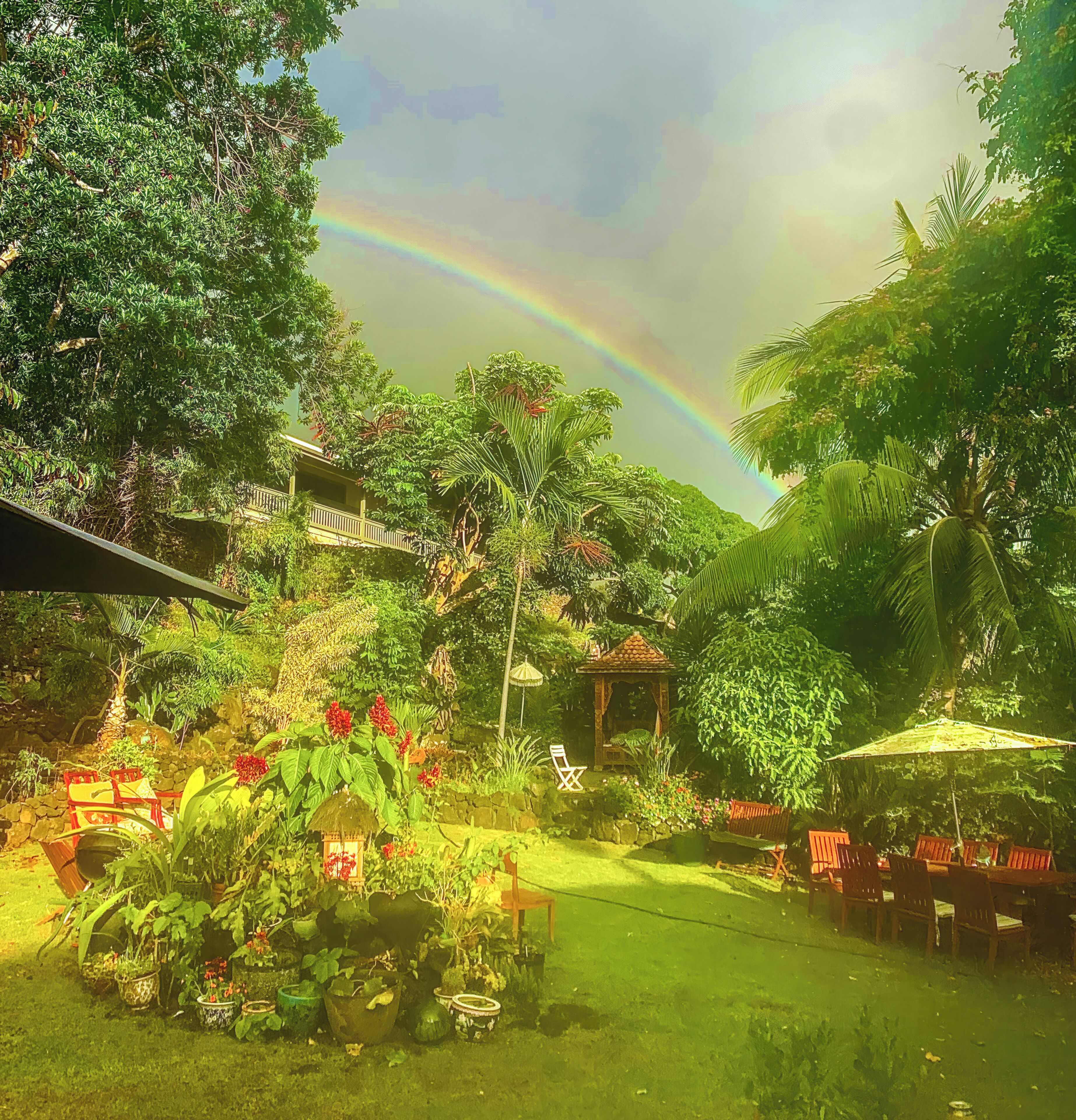 A lush garden with a gazebo, outdoor seating, and a rainbow in the background.