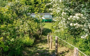 Ein Weg, der zu einem Gebäude mit grüner und weißer Fassade führt, umgeben von üppigem Grün und weißen blühenden Büschen.