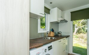 A compact kitchen with a Bosch washing machine, a stainless steel sink, and a window with a view of greenery. - Camper Foundation Sophie (Burgh-Haamstede)