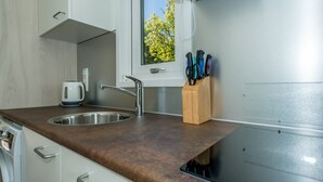 Une cuisine équipée d’un évier à deux bacs, d’une bouilloire et d’une fenêtre donnant sur les arbres.