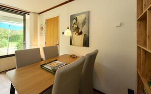 En matplats med ett träbord, fyra stolar, en inramad tavla på väggen och ett fönster med utsikt över grönområden.