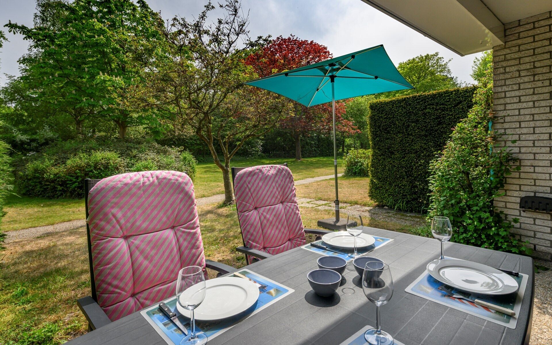 An outdoor dining area with a table set for two, chairs, and a blue umbrella.