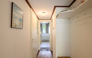 En smal hall med trägolv, en taklampa och en dörr som leder till ett rum med ett element och ett fönster med gardiner.