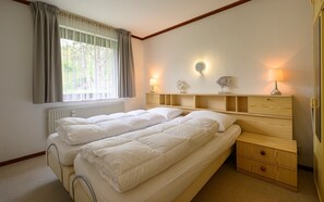 A bedroom with a bed, bedside tables, a radiator, and a window with curtains. - Apartment Torenhoeve 53 at a quiet holiday hotelcomplex (Burgh-Haamstede)