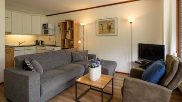 Een woonkamer met een grijze bank, een houten salontafel, een televisie en een keuken op de achtergrond.