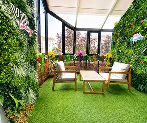 A room with two wooden chairs, a small table, and a green artificial turf floor. - A beautiful, chic, and cozy home near Paris. (Créteil)