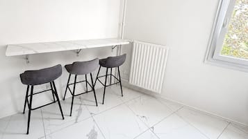 Een moderne keuken met een wit aanrecht, drie barkrukken, een hanglamp en een raam met uitzicht.
