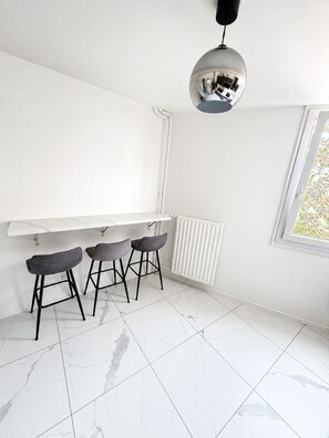 A modern kitchen with a white countertop, three bar stools, a pendant light, and a window with a view. - A beautiful, chic, and cozy home near Paris. (Créteil)