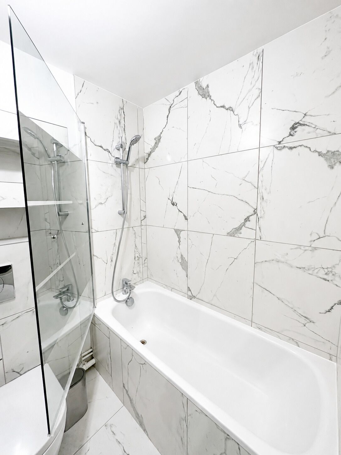 Un baño moderno con ducha envuelta en vidrio, una bañera independiente y baldosas con diseño de mármol.
