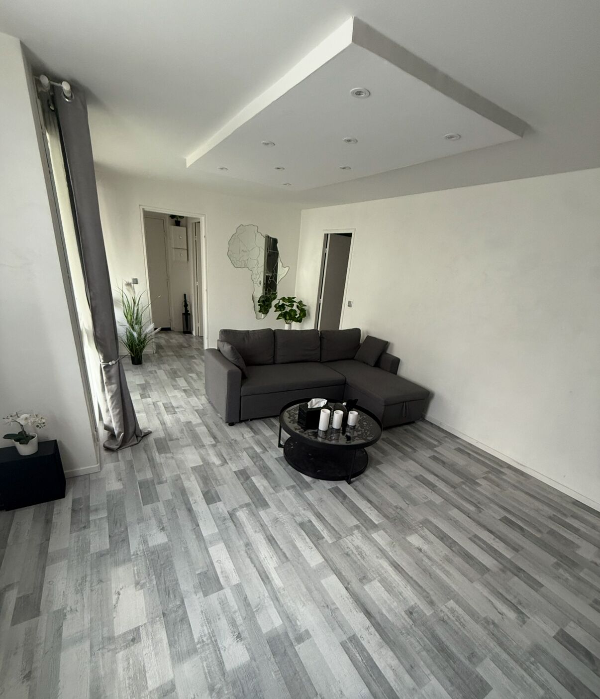 Een moderne woonkamer met een hoekbank, een ronde salontafel en een groot raam.