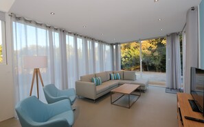 Ein modernes Wohnzimmer mit einem Ecksofa, zwei Sesseln, einem Couchtisch und einem Fernseher.