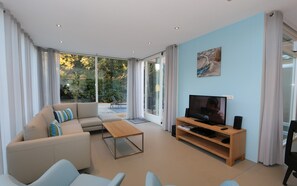 Ein modernes Wohnzimmer mit einer Couch, einem Couchtisch, einem Fernseher und einer Schiebeglastür, die auf einen Balkon führt.